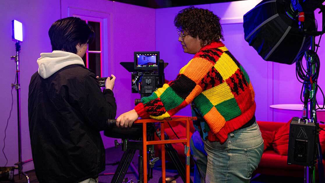 Two students face monitor on camera and on film set.