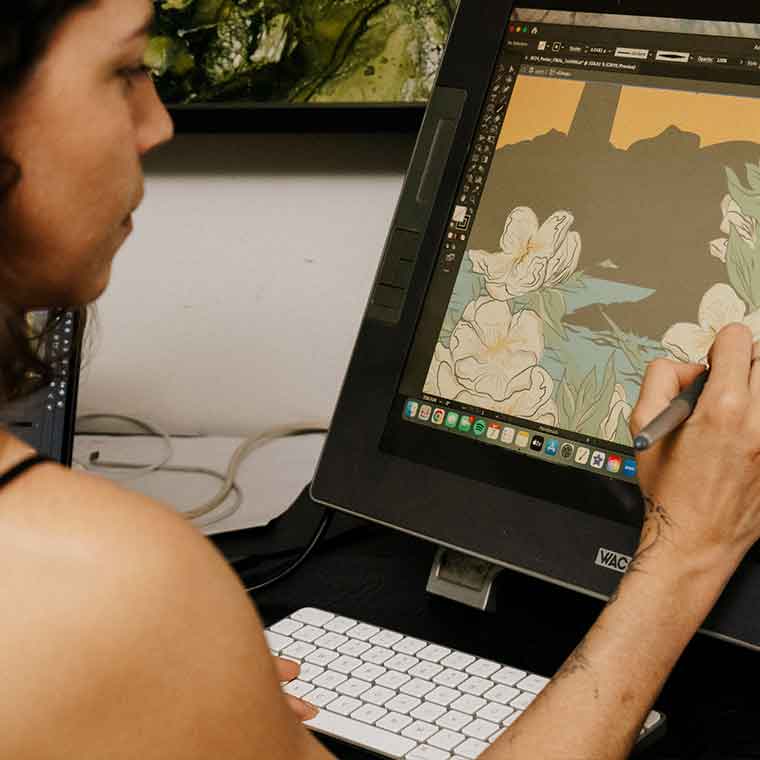 A woman is using a stylus to draw directly onto a Wacom screen. The woman has a keyboard in front of her and is using the keys while drawing.