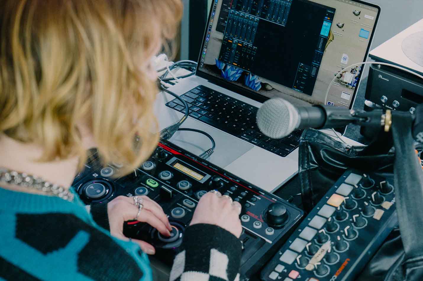 Woman stands over mixing console and microphone in front of a laptop with mixing software