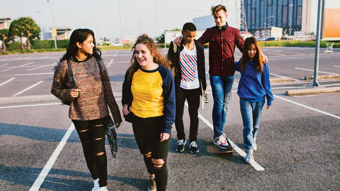 A group of young people engaged in conversation walk across an outdoor asphalt basketball court