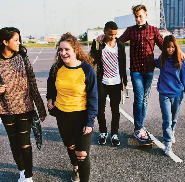 A group of young people engaged in conversation walk across an outdoor asphalt basketball court
