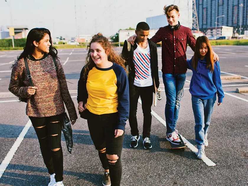 A group of young people engaged in conversation walk across an outdoor asphalt basketball court