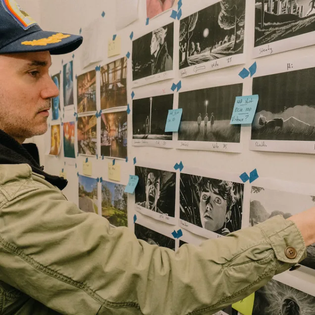 Man wearing cap and hoodie, back to camera, stands in front of wall covered with movie illustrations - storyboard/script. SAE MASTER OF CREATIVE INDUSTRIES POSTGRAD, MARK GAMBINO