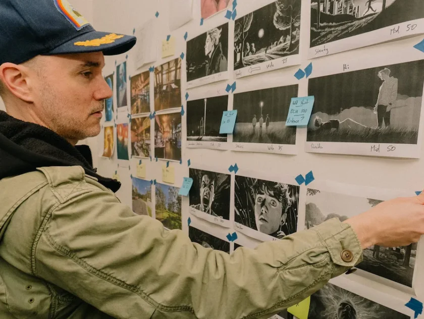 Man wearing cap and hoodie, back to camera, stands in front of wall covered with movie illustrations - storyboard/script. SAE MASTER OF CREATIVE INDUSTRIES POSTGRAD, MARK GAMBINO