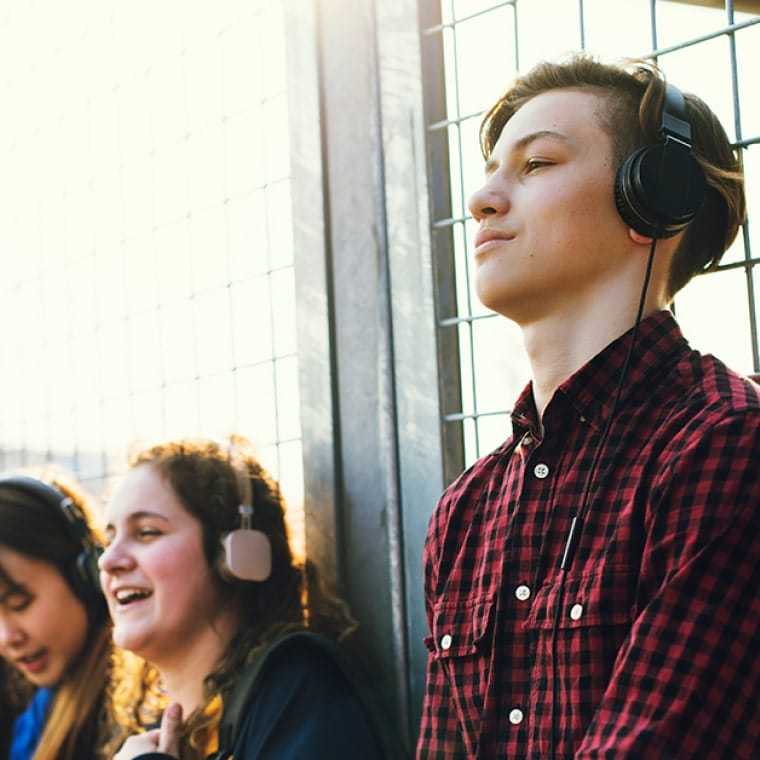 A young man wearing over-ear headphones, with four other students in the background desktop