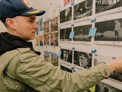 Man wearing cap and hoodie, back to camera, stands in front of wall covered with movie illustrations tile thumbnail