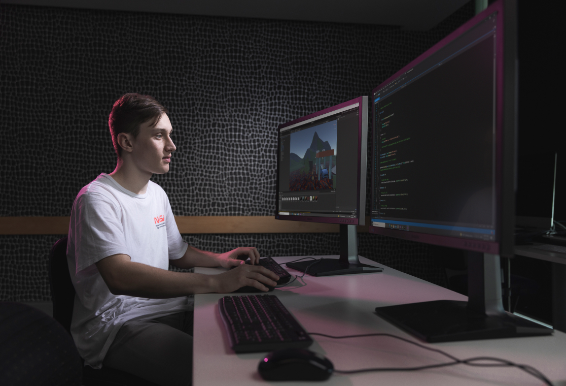 Male students with NASA t-shirt working on two desktop monitors