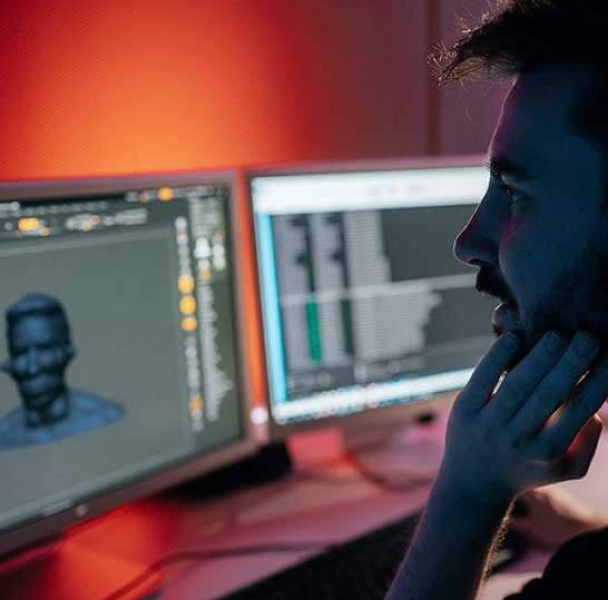 A male student sitting at a work desk, viewing two monitors