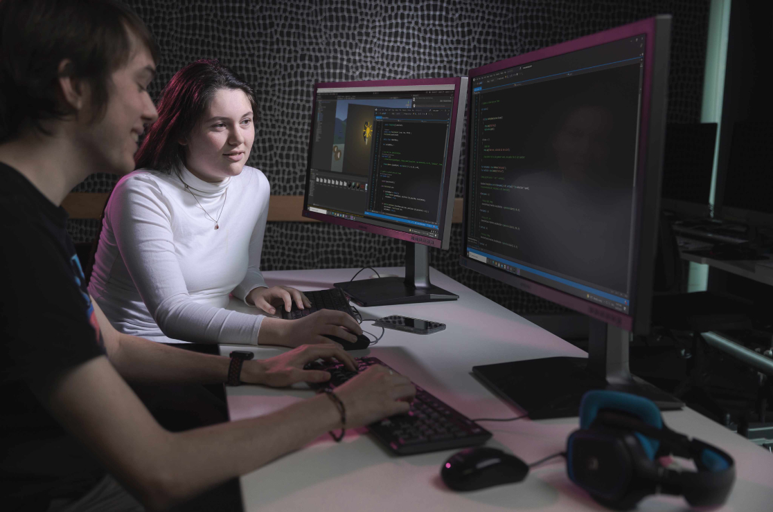 Male and female student working together on two large monitors