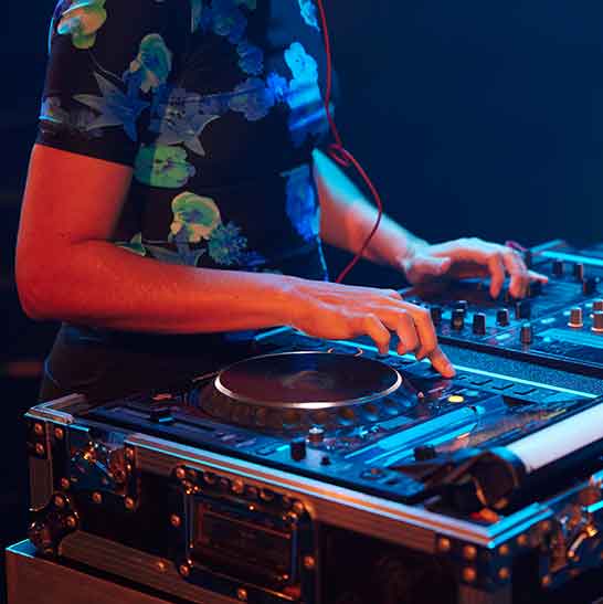 Person in front of a DJ mixing console and decks.