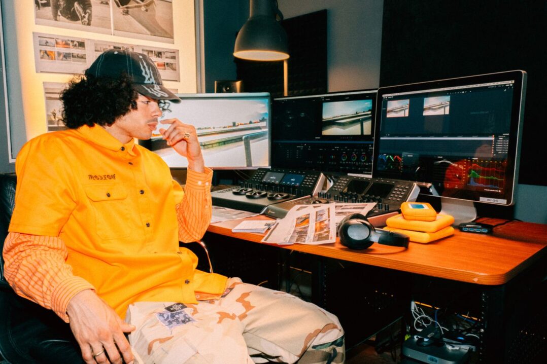 A man with a hat and curly hair sitting in front of a desk with three computer monitors | VFX and Virtual Production