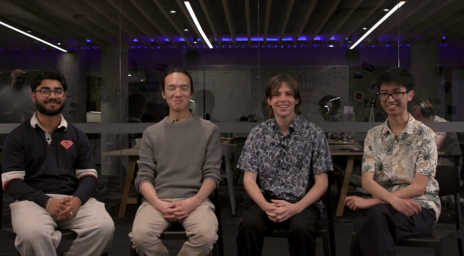 four young men sit in a row on chairs smiling at the camera