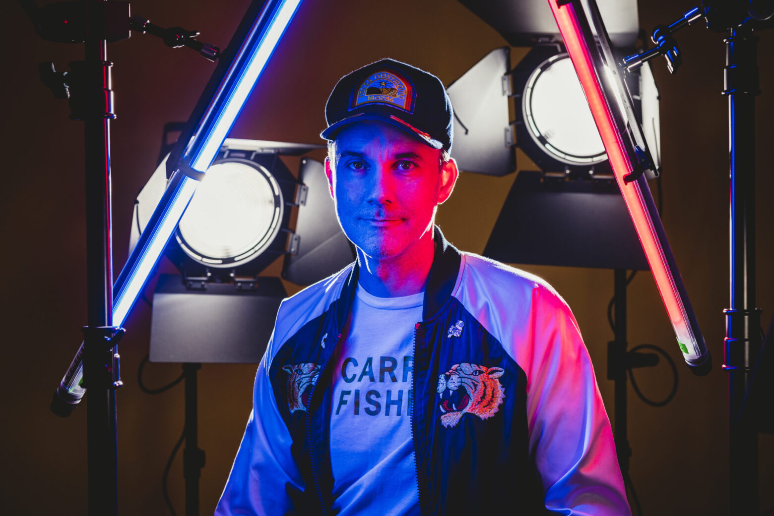 man in hat and jumper appears in multi colour lighting on film set