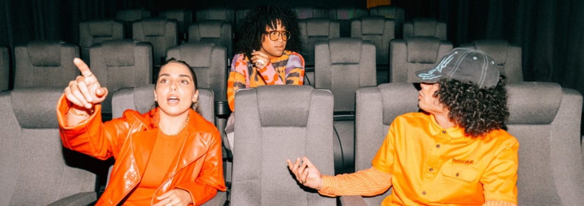 Three students sitting in a theatre room with one pointing towards the screen