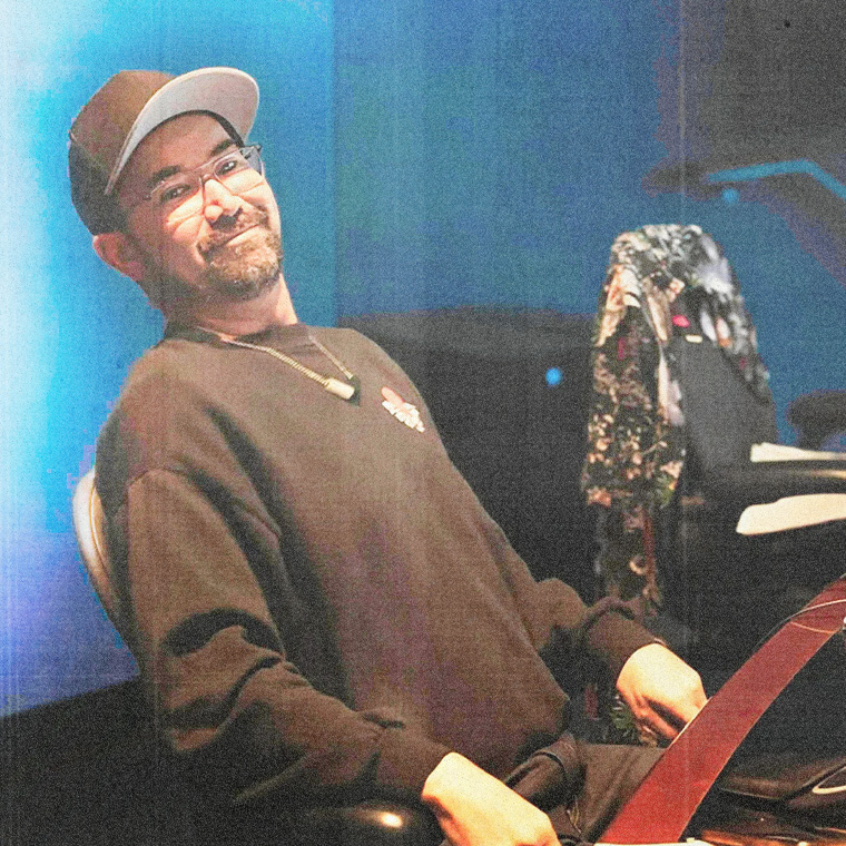 Man wearing cap and glasses leans back in office chair. Smiling at camera.