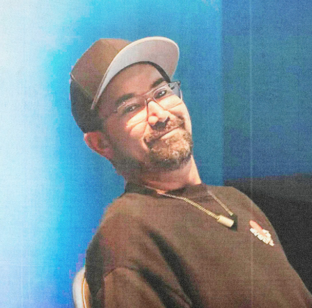 Man in cap and glasses smiles at camera.