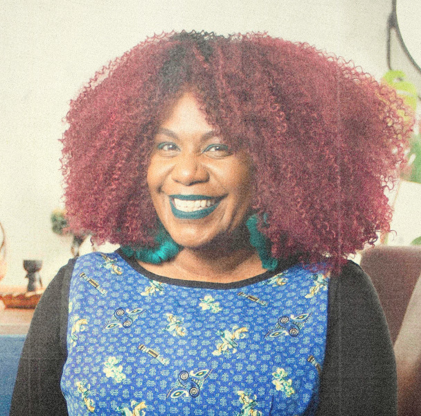 Woman with wearing green earrings, lipstick and eye makeup smiles at camera.