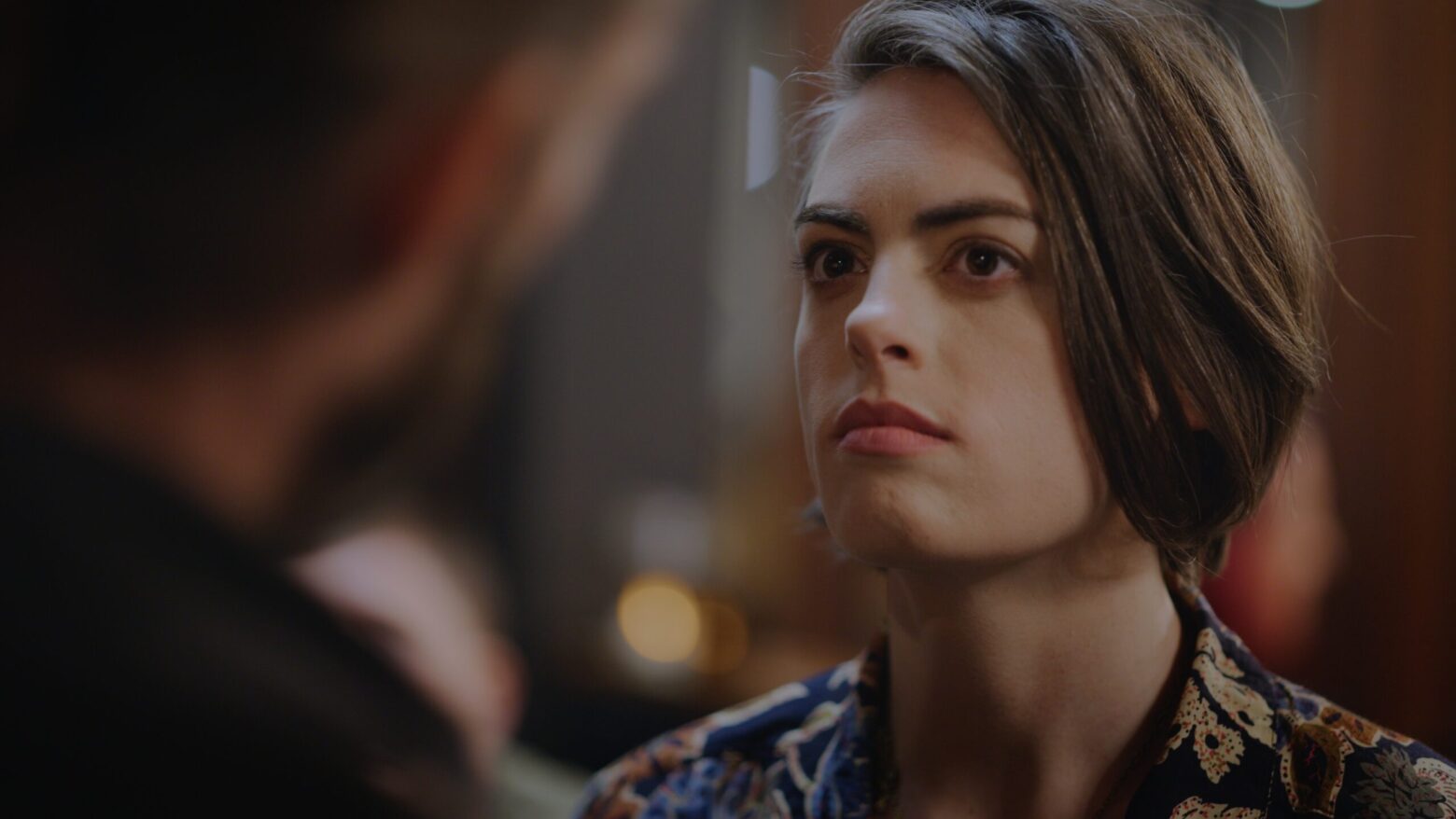 over shoulder photo of woman looking to her right. she has a short bob and looks strained.