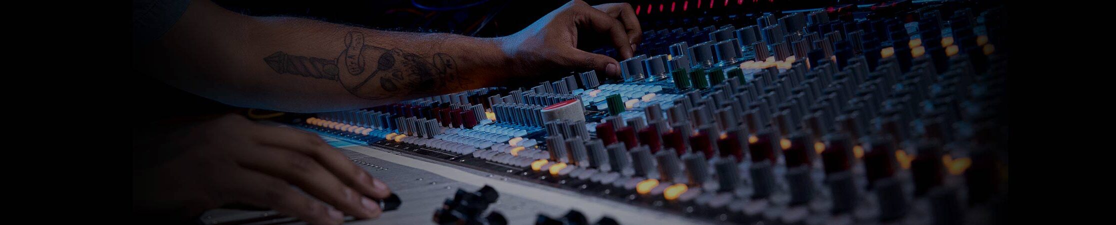 Man sitting at mixing audio console. Hands hold knobs and sliding fader.