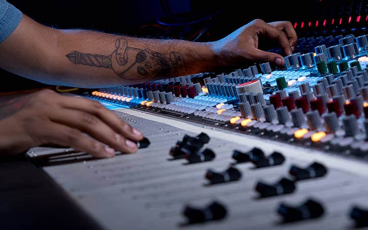 Person sitting at mixing audio console. Hands hold knobs and sliding fader.