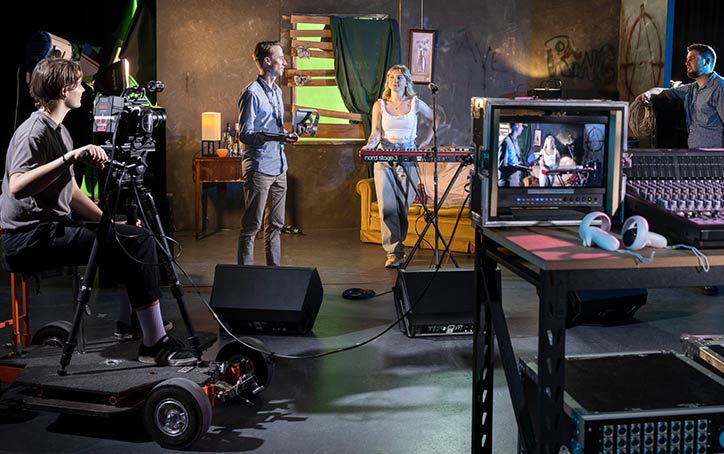 Group of people in studio. Cameraman. Keyboard musician. Camera operator. Monitor and Mixing board.