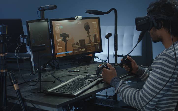 Person wearing virtual headset in front of virtual environment displayed on monitor