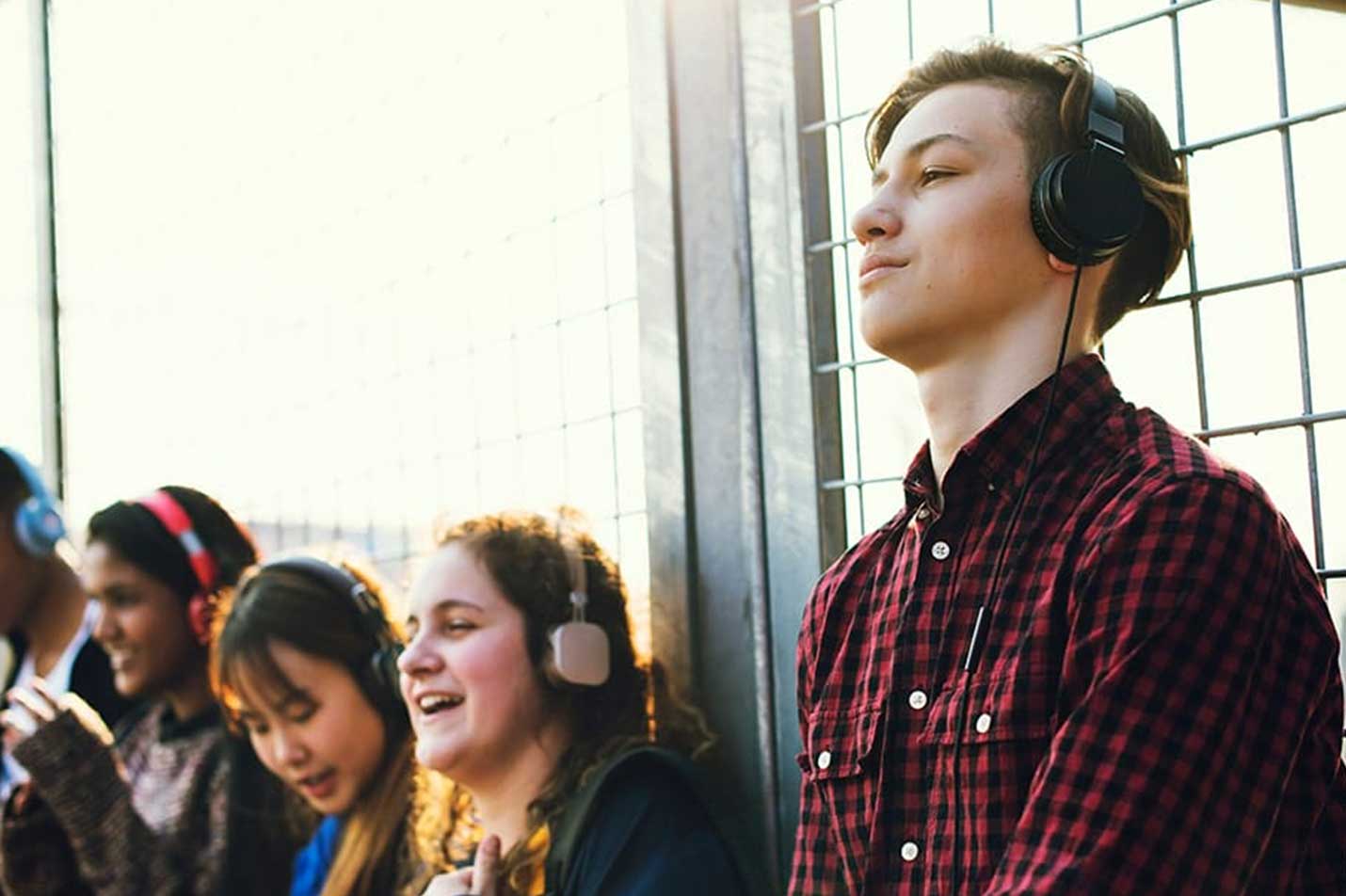 A young man wearing over-ear headphones, with three other students in the background also wearing headphones