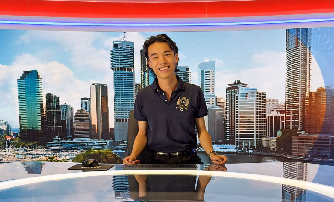 man poses at news desk in front of city skyline