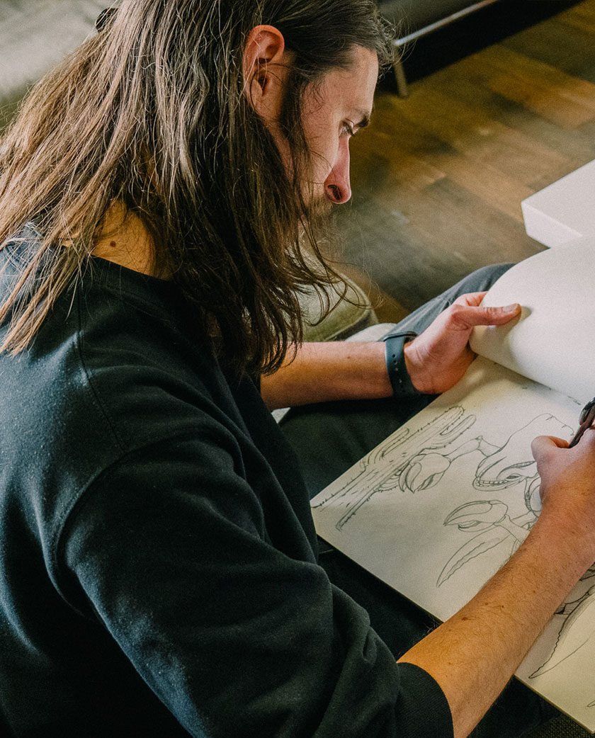 A man is holding a sketchpad and drawing on the pad with pen and looking down