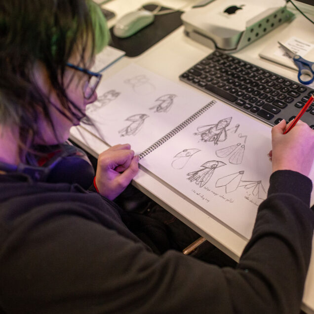 Person drawing in a sketch pad on desk in front of keyboard