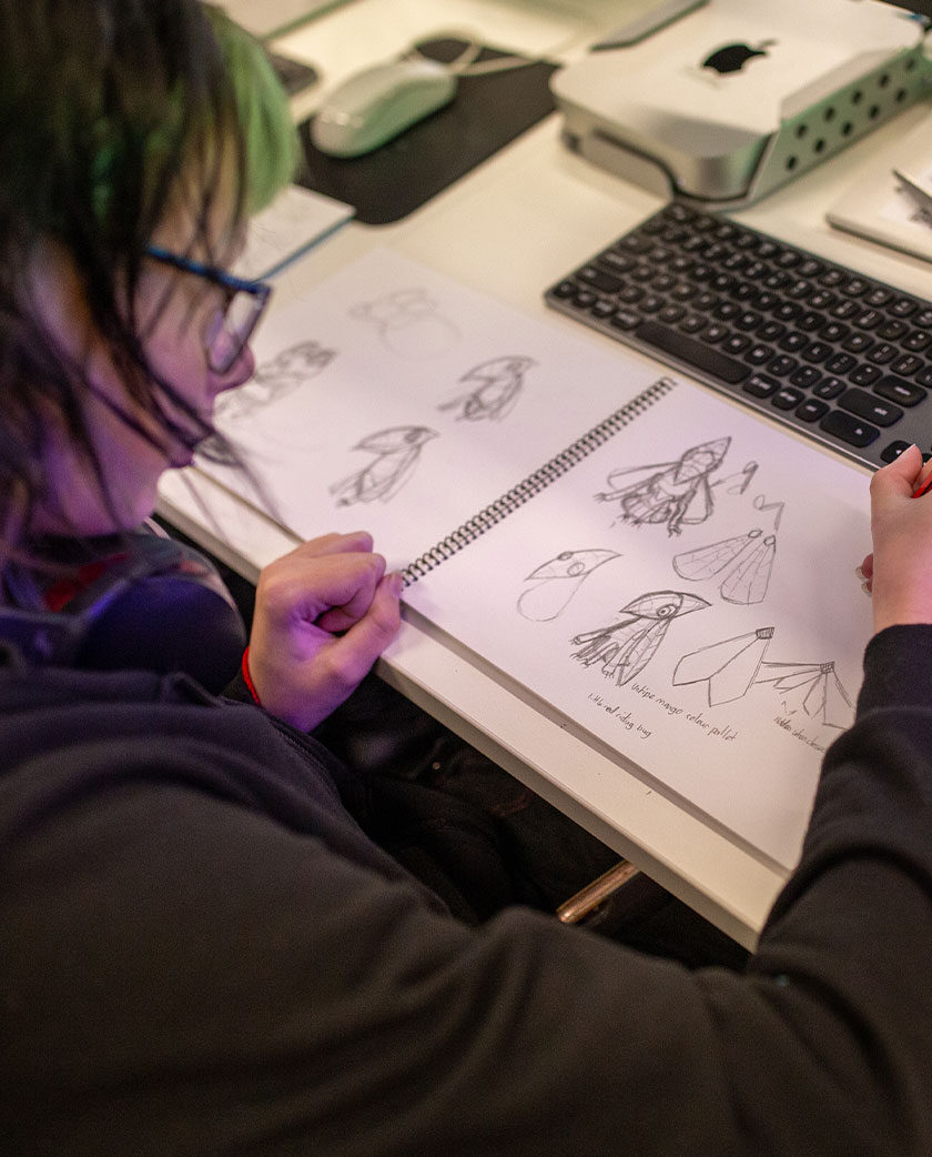 Person drawing in a sketch pad on desk in front of keyboard