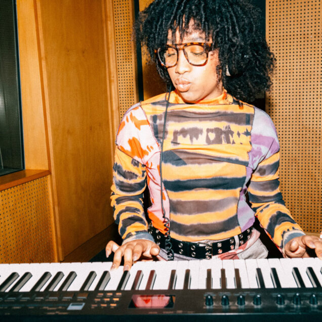 Woman wearing glasses standing above and looking down at keyboard. She appears to be playing the keyboard - her fingers are on the keys.