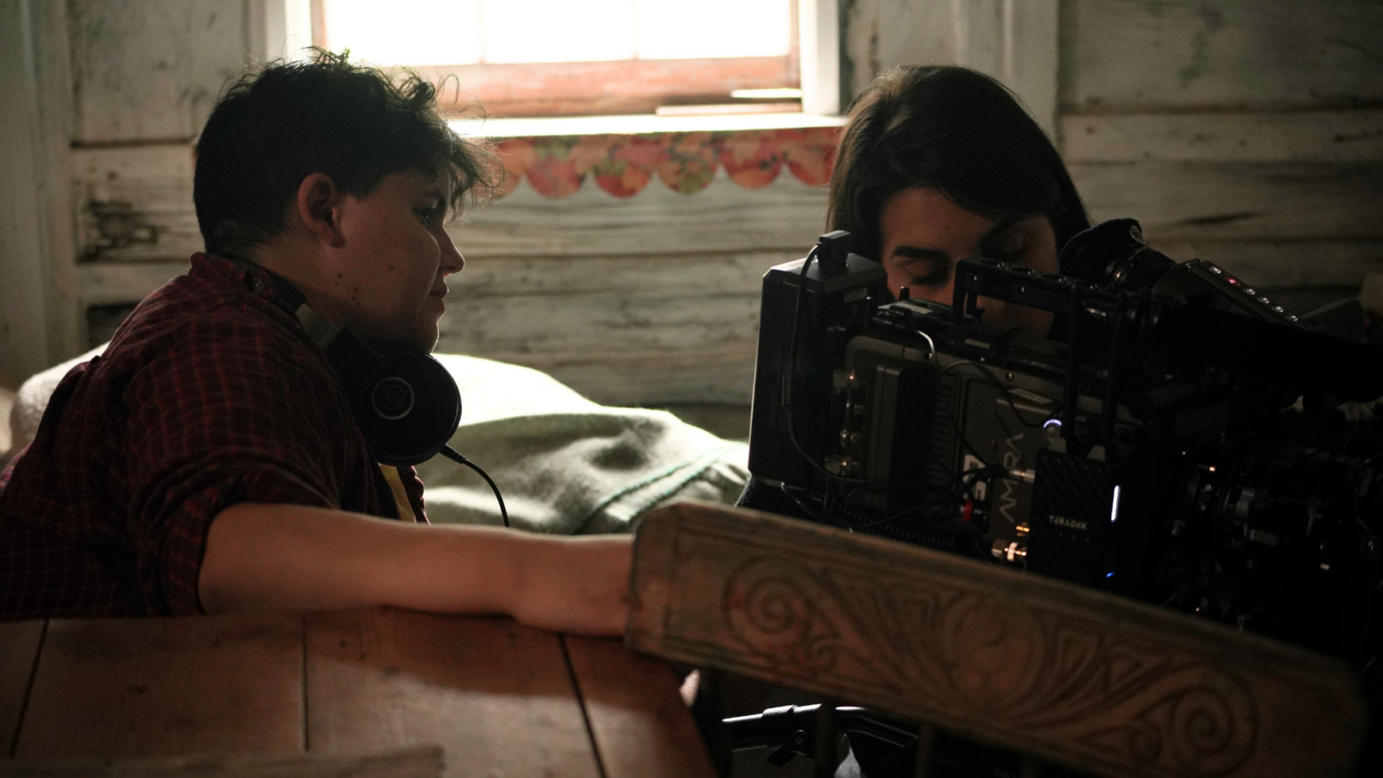 person in checked shirt with earphones around their neck and another person look at camera in an old cottage room