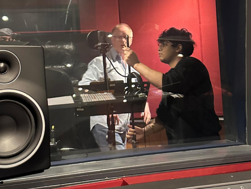 woman with curly hair and glasses helps middle aged man with microphone in recording booth