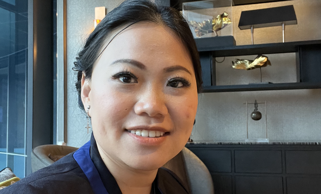 woman of east asian background in front of office background wearing corporate clothes smiling