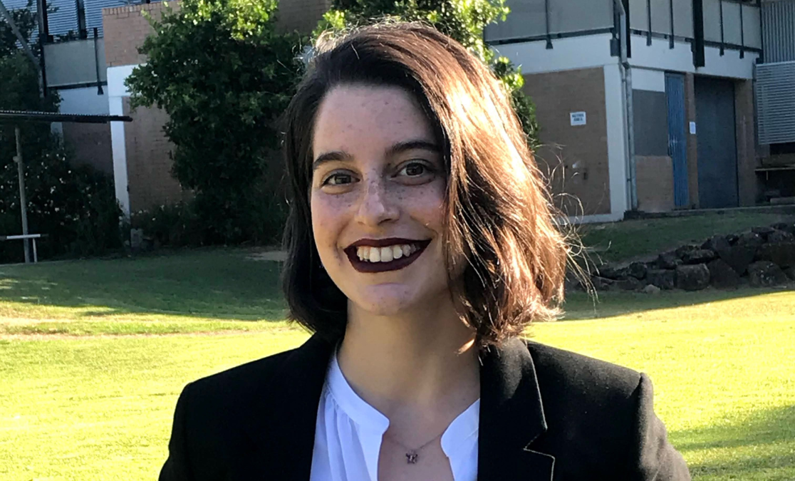 caucasian-looking woman with bob haircut and dark lipstick in a blazer in front of a green lawn