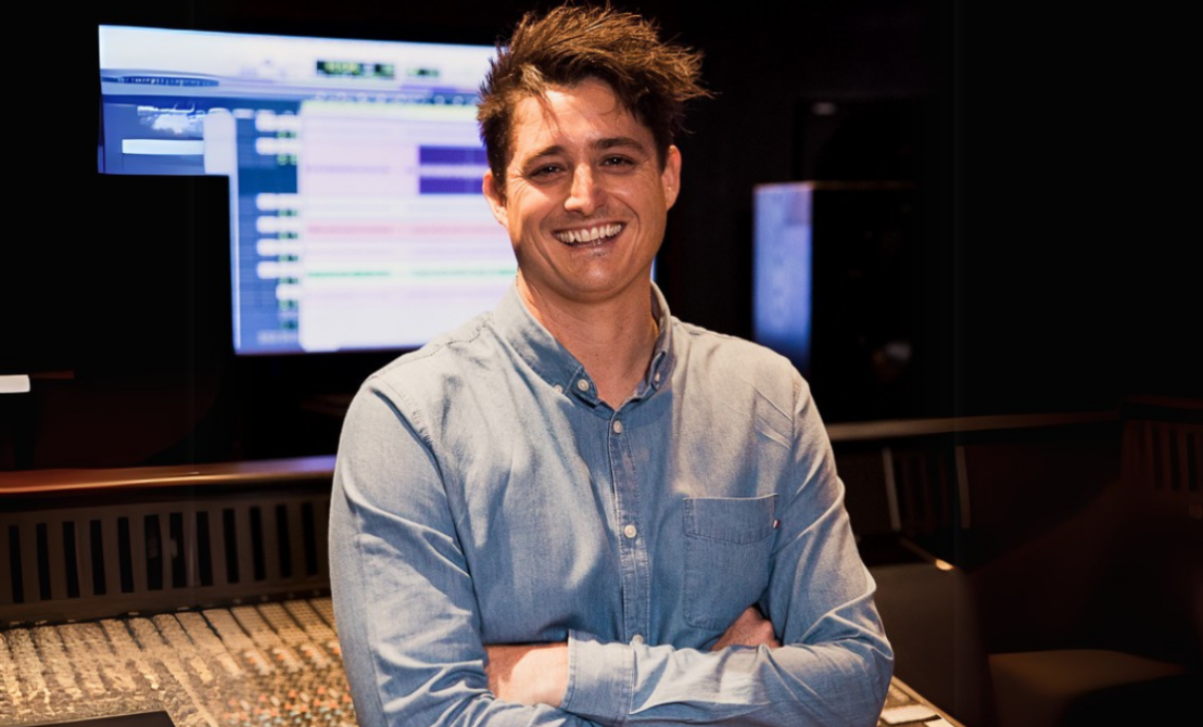 man smiles with crossed arms in front of studio backdrop