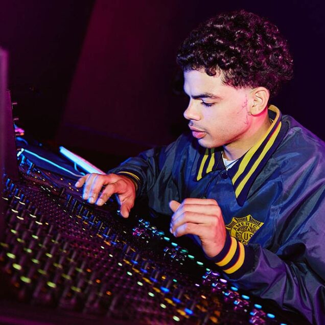 A young male student operating a mixing desk in a room with dark lighting 1224x687