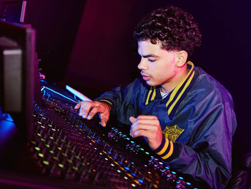 A young male student operating a mixing desk in a room with dark lighting 1224x687
