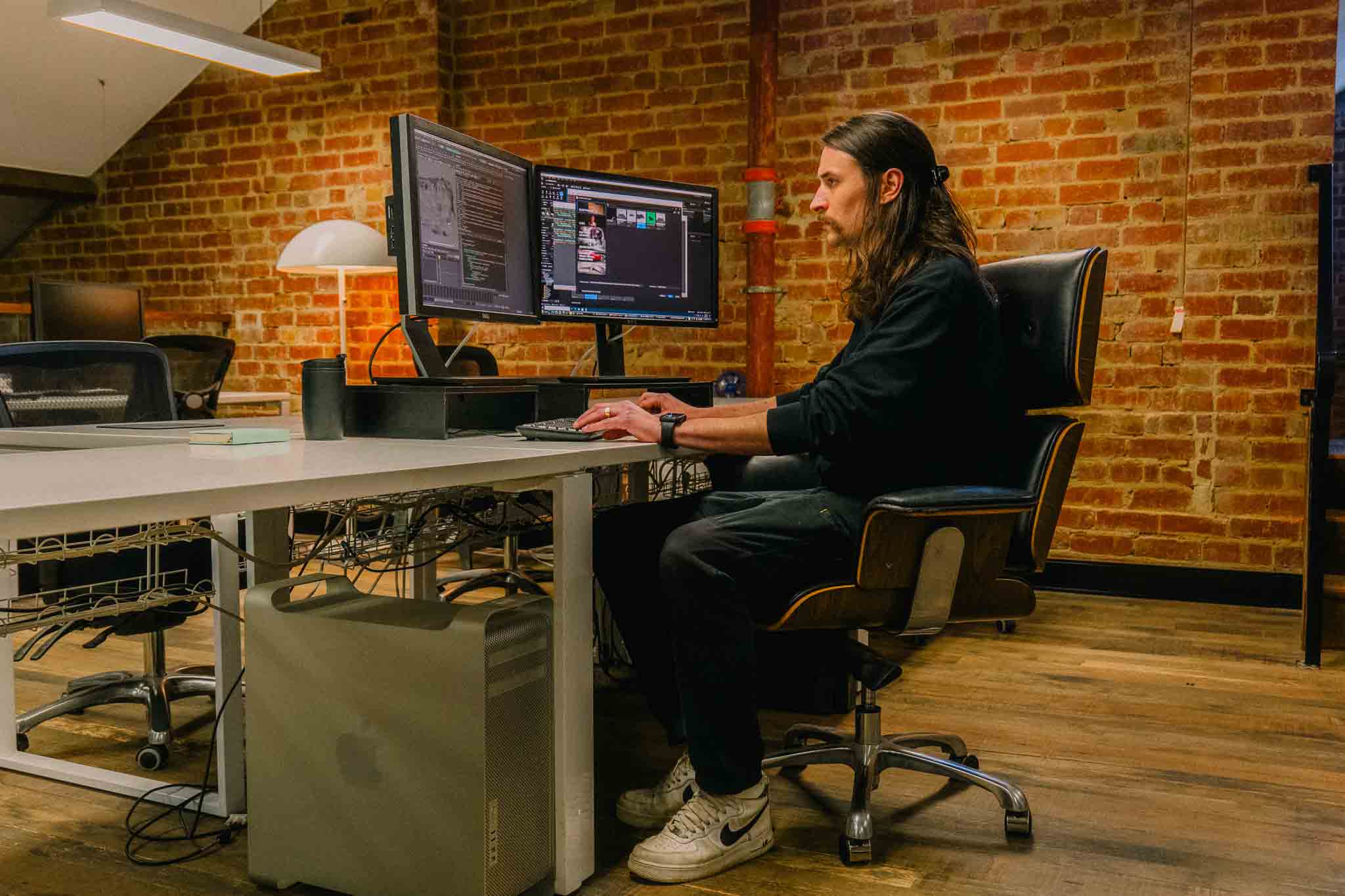 SAE Bachelpor of Animation alumni Blake Sala sitting at a desk with two monitors in a room with red brick walls