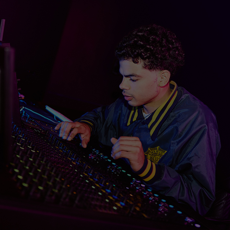 A young male student operating a mixing desk in a room with dark lighting 760x760