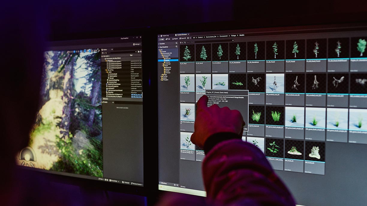 A hand pointing towards a computer monitor in a games studio with low lighting