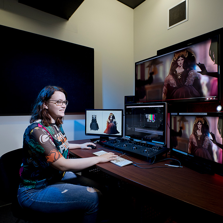 A female games development student working in a games studio on a desktop computer with several large monitors