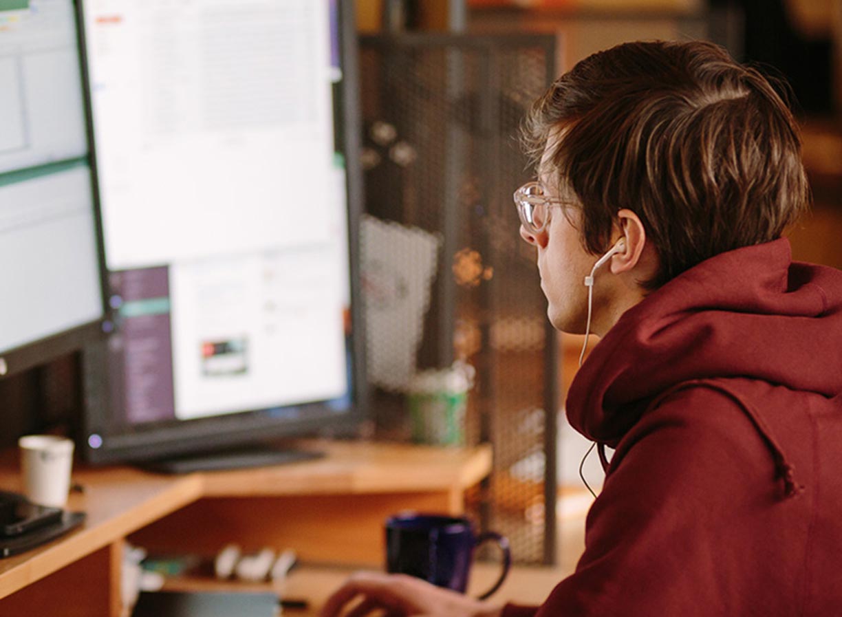 A male ICT project manager wearing headphones and working at a desk with several monitors - Information Technology