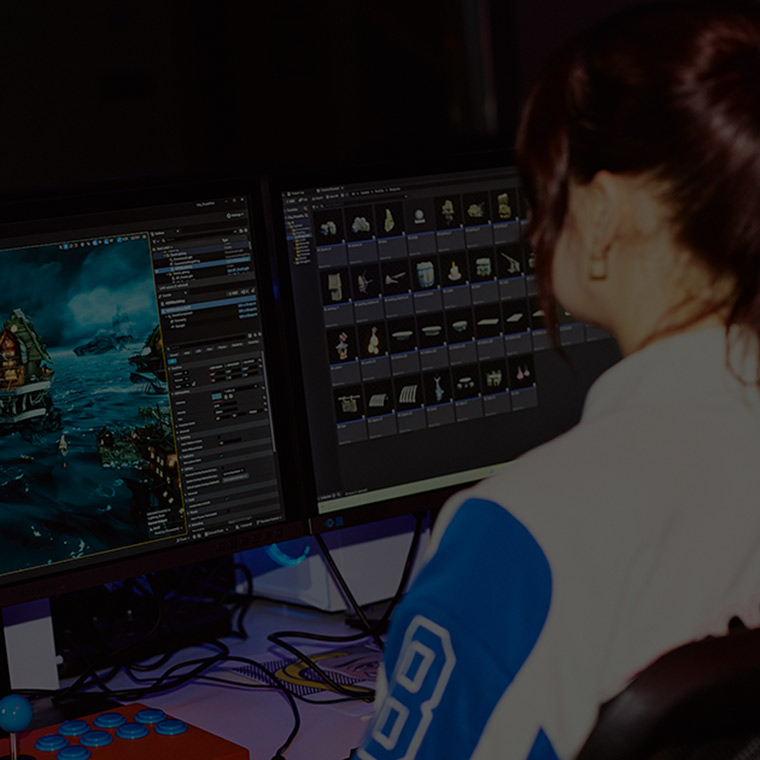 A woman with red hair in a ponytail facing away from camera, working with games software on a desktop monitor - with black overlay