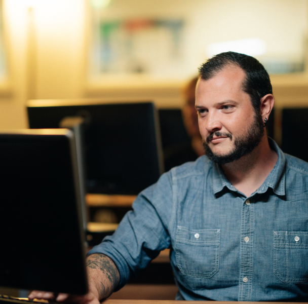 A man with short hair and facial hair working in a studio with desktop computers