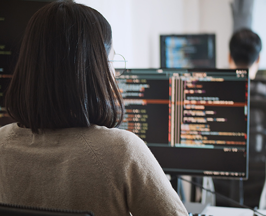 A woman with short hair and glasses working at a desktop computer - Diploma of Cyber Security