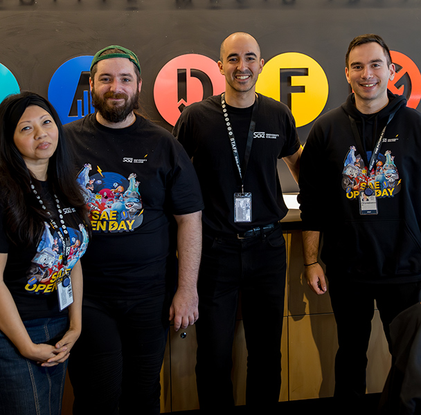Four SAE University College student advisors wearing lanyards, standing in front of a reception desk
