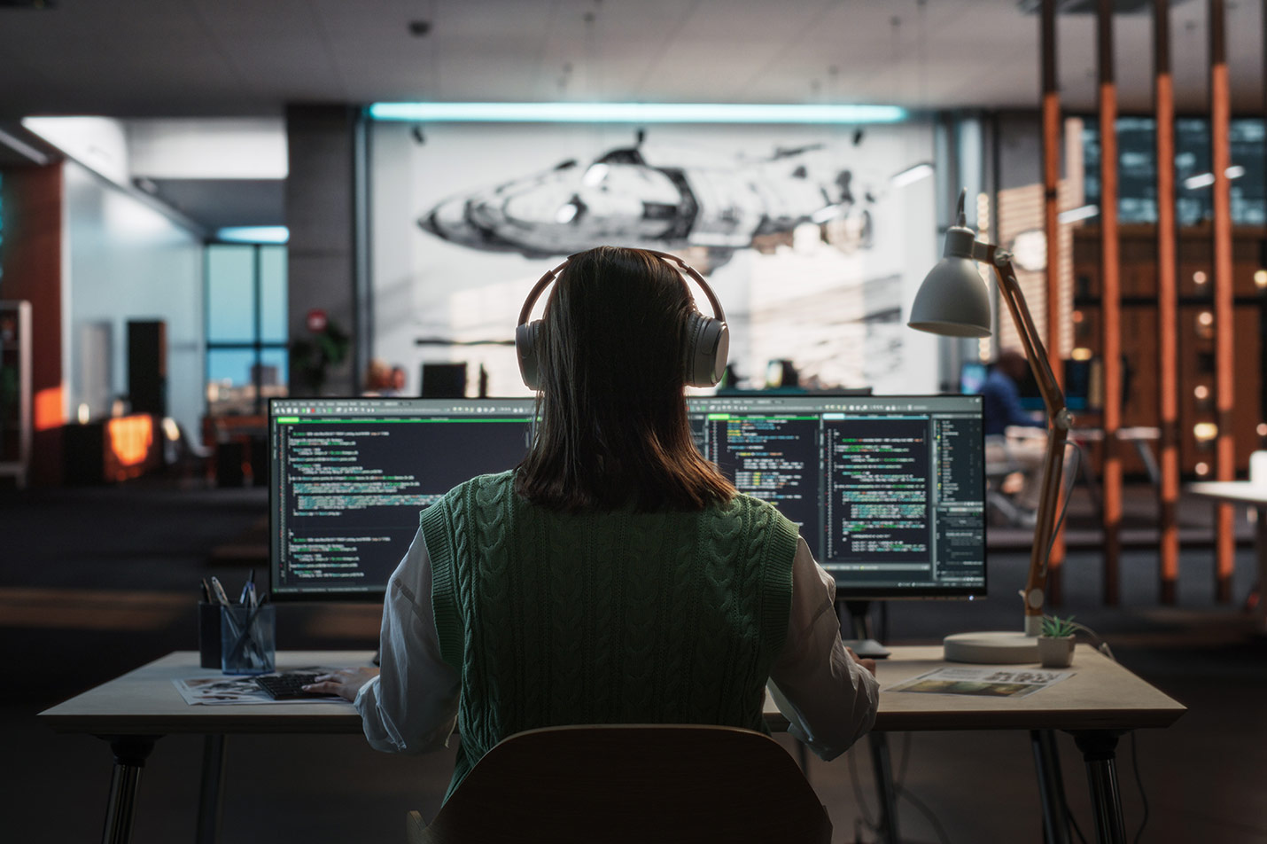 A women wearing a sweater and over ear headphones, working on two computer monitors - MIT scholarship desktop header image
