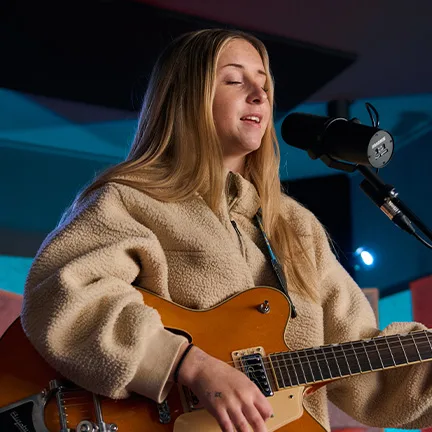 Woman sings into a microphone while playing an acoustic guitar